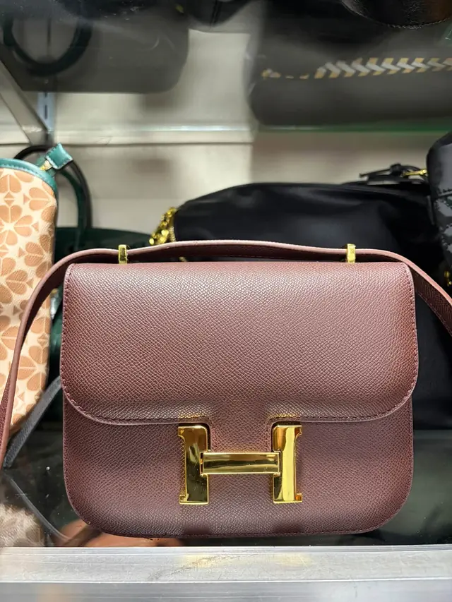 Oxblood grained-leather flap bag with a large gold clasp and a slim crossbody strap